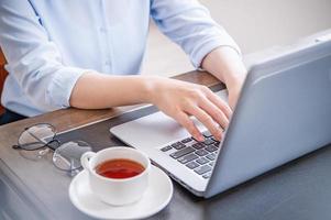 conceito de negócios. mulher de camisa azul digitando no computador com café na mesa do escritório, luz de fundo, efeito de brilho do sol, close-up, vista lateral, copie o espaço foto