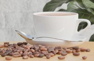xícara de café branco e grãos de café na mesa de madeira com fundo de parede de tijolo branco e planta.