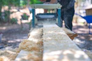 trabalhador esfrega a grande placa de madeira longa com máquina de polir no jardim. foto