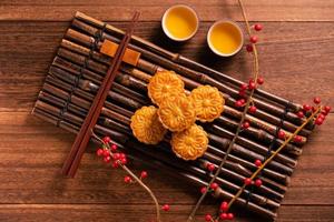 bolo de lua configuração de mesa de bolo de lua - pastelaria tradicional chinesa com xícaras de chá em fundo de madeira, conceito de festival de meio outono, vista superior, configuração plana. foto