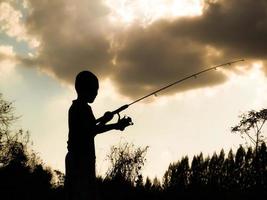 silhueta de uma criança pescando o tempo feliz das crianças no meio da natureza ao pôr do sol foto
