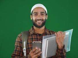 menino muçulmano jovem estudante com livros sobre fundo de tela verde. foto