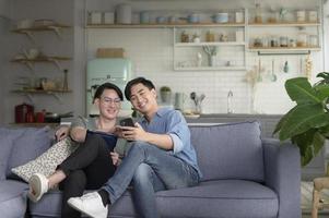 jovem casal gay sorridente usando smartphone e relaxando na sala de estar em casa, lgbtq e conceito de diversidade. foto