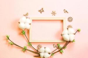 moldura feita de flores de algodão, delicadas folhinhas de botões abertos em ramos-brotos em um fundo rosa e borboletas de madeira esculpida, pássaros, ornamentos. primavera, vida nova, ternura. espaço de cópia foto