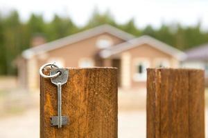 a chave da casa está pendurada na cerca. fundo da casa de campo. sonho da casa, construção, projeto, entrega do projeto, mudança de casa nova, hipoteca, aluguel e compra de imóveis. espaço de cópia foto