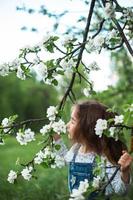 uma menina bonitinha de 5 anos em um pomar de maçãs brancas florescendo na primavera. primavera, pomar, floração, alergia, fragrância primaveril, ternura, cuidado com a natureza. retrato foto