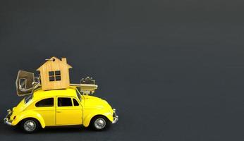 carro de brinquedo amarelo com a chave da casa no telhado em um fundo preto. mudar para uma casa nova, hipoteca, comprar um apartamento, táxi. espaço de cópia foto