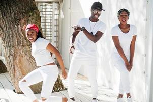 três elegantes amigos afro-americanos, usam roupas brancas. moda de rua de jovens negros. homem negro com duas garotas africanas dançando estilo gangsta rap. foto