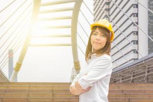 construção e manutenção pensam grande conceito, arquiteta feminina no capacete amarelo com fundo da cidade foto