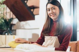 retrato da pequena empresária asiática de pequenas empresas ou dona da loja colocando pano em embalagens de papel para embalar o pedido do cliente preparando-se antes da entrega do envio. mulher de vendedor de sucesso feliz. foto