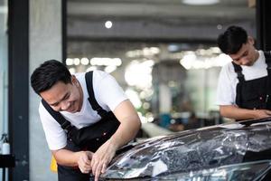 especialista em proteção de pintura de filme de detalhamento de dois asiáticos cortando e embrulhando carro em showroom de garagem, instalação de revestimento protetor e automóvel de polimento para conceito de negócio de serviço de manutenção de veículos foto