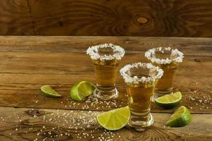 três doses de tequila de ouro no fundo de madeira foto