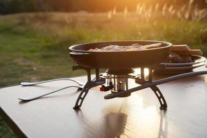 piquenique na natureza, salsicha frita em uma frigideira para camping foto