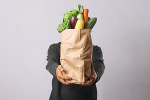 close-up da sacola de compras com legumes segurando pelas mãos para o conceito de entrega de compras on-line foto