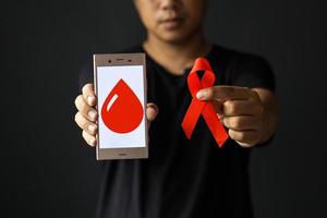 dia mundial da aids ou dia mundial do diabetes com mãos masculinas segurando fita vermelha de conscientização da aids e símbolo de sangue. conceito de saúde e medicina.