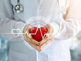 médico com estetoscópio e forma de coração vermelho com batimento cardíaco ícone nas mãos no fundo do hospital foto