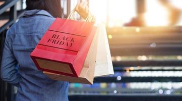 vista traseira da mulher segurando a sacola de compras de sexta-feira preta enquanto subia escadas ao ar livre no fundo do shopping foto