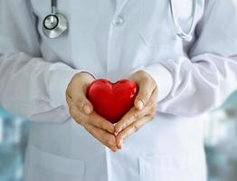 médico com estetoscópio e forma de coração vermelho nas mãos no fundo do hospital foto