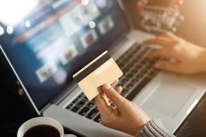 conceito de compras on-line. mulher segurando o cartão de crédito de ouro na mão e compras on-line usando o laptop em casa. foto