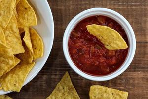 chips de tortilha dentro da tigela com salsa na mesa de madeira rústica foto