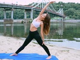 jovem apta em roupas esportivas em diferentes asanas de ioga ao ar livre na praia à beira do rio. conceito de ioga e esporte foto