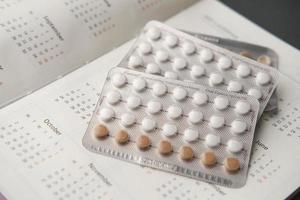 pílulas anticoncepcionais, calendário e bloco de notas na mesa foto