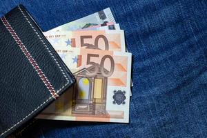 dinheiro do euro, notas de euro dentro da carteira de couro preto sobre fundo de jean. foto