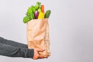 sacola de compras de supermercado com legumes segurando pelas mãos para o conceito de entrega de compras on-line foto