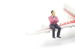 empresário em miniatura sentado na asa do avião no fundo branco