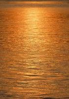 movimento de borrão leve da reflexão da luz solar dourada colorida na superfície do rio na hora do pôr do sol no quadro vertical foto