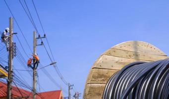 bobina de madeira de cabo elétrico com fundo desfocado do grupo de eletricistas trabalhando em postes de energia contra o céu azul foto