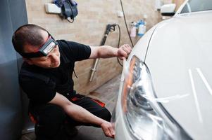 trabalhador na garagem de detalhamento colocou capa de filme anti-cascalho de poliuretano no carro de luxo branco. foto