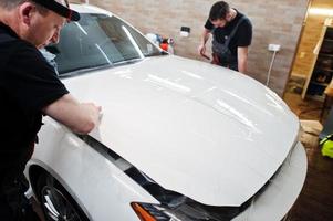 trabalhador na garagem de detalhamento colocou capa de filme anti-cascalho de poliuretano no carro de luxo branco. foto