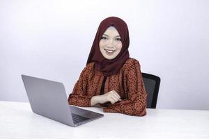 jovem islão asiático está sentado desfrutar e sorrindo ao trabalhar no laptop em fundo branco. foto