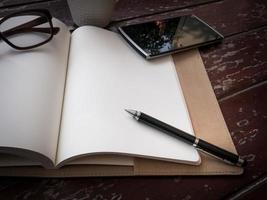 espaço de trabalho com óculos, caneta, smartphone e xícara de café, papel de nota e caderno na velha mesa de madeira foto