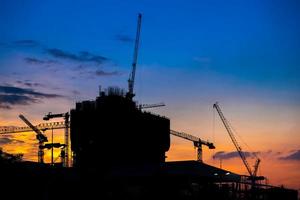 guindastes de construção industrial e silhuetas de construção sobre o pôr do sol foto