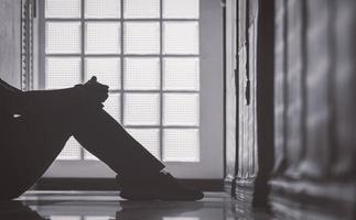 seção baixa de mulher deprimida sentada sozinha com abraçando os joelhos no corredor do apartamento em estilo discreto e monocromático, conceito de saúde mental foto