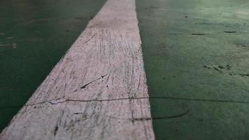 close-up de uma linha branca rachada desenhada em um piso quebrado em verde no campo de esportes público. foto