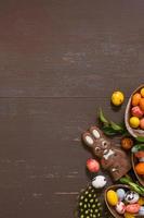 fundo de conceito de caça de páscoa com ovos de chocolate e coelho no espaço de cópia de mesa de madeira. vista de cima foto