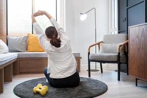 atraente e saudável jovem asiática fazendo exercícios em casa durante o treino em roupas confortáveis em um tapete em sua sala de estar, conceito de estilo de vida saudável