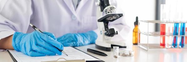 jovem cientista asiático trabalhando olhando através de um microscópio fazendo pesquisas para analisar uma amostra de experimentos em um laboratório forense.