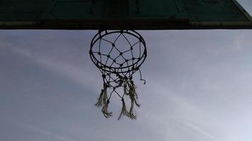 vista inferior da cesta de basquete velha verde escura e rede quebrada com um fundo escuro do céu matinal no campo de esporte público. foto