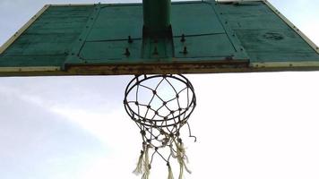 vista inferior da cesta de basquete velha verde escura e rede quebrada com um fundo escuro do céu matinal no campo de esporte público. foto