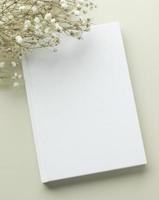 maquete de capa em branco de livro branco em um fundo bege com flor seca, postura plana, maquete