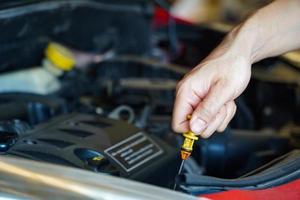 mecânico asiático reparando carro com capô aberto, vista lateral do mecânico verificando nível de óleo do motor em um carro com capô aberto foto