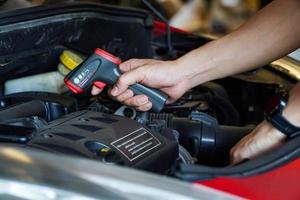 a mão do técnico segura um termômetro digital, que mede o calor do motor. medição de temperatura do motor no serviço de carro foto