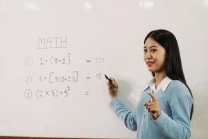 professora asiática está ensinando os alunos na sala de aula enquanto aponta para números no quadro branco.