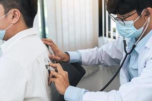médico asiático está usando um estetoscópio para ouvir os batimentos cardíacos do paciente. foto