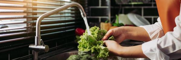 mulher de mãos asiáticas lavando salada de legumes e preparação de alimentos saudáveis na cozinha. foto