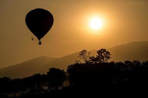 a silhueta do balão de ar quente voando no céu durante a vista do pôr do sol. foto